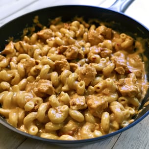 Skillet of creamy chipotle chicken mac and cheese, with elbow macaroni and browned chicken pieces coated in a glossy orange cheese sauce with visible red pepper flecks.
