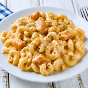 Plate of buffalo chicken mac and cheese made with elbow macaroni in a creamy orange cheese sauce, mixed with bite-size chicken pieces and sprinkled with green herbs on a white plate.