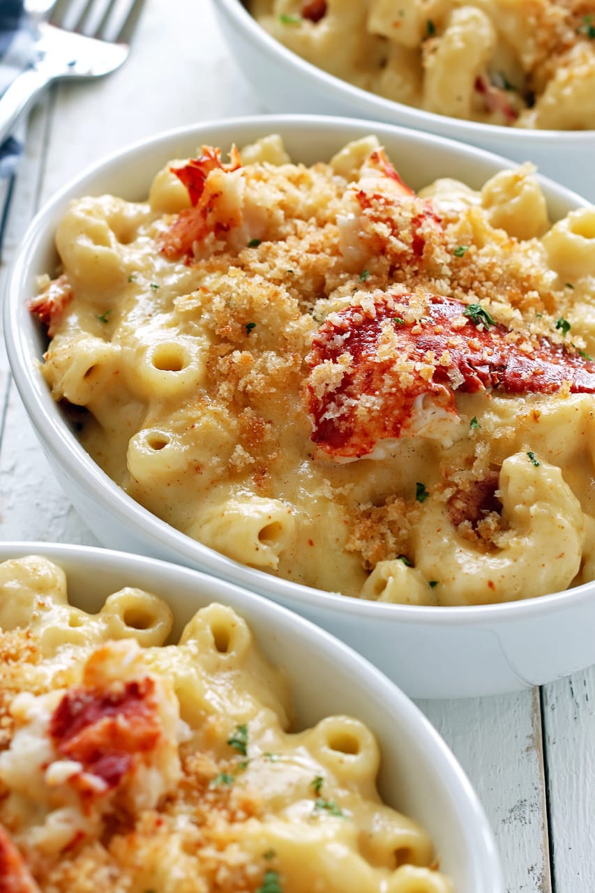 Close-up of lobster mac and cheese served in white bowls, with creamy cavatappi coated in a rich cheese sauce and topped with red lobster pieces, golden toasted breadcrumbs, and a light sprinkle of herbs.